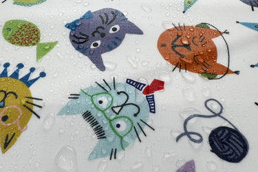 Water droplets on laminated cat fabric. Fabric has a cream background with colorful cat faces.